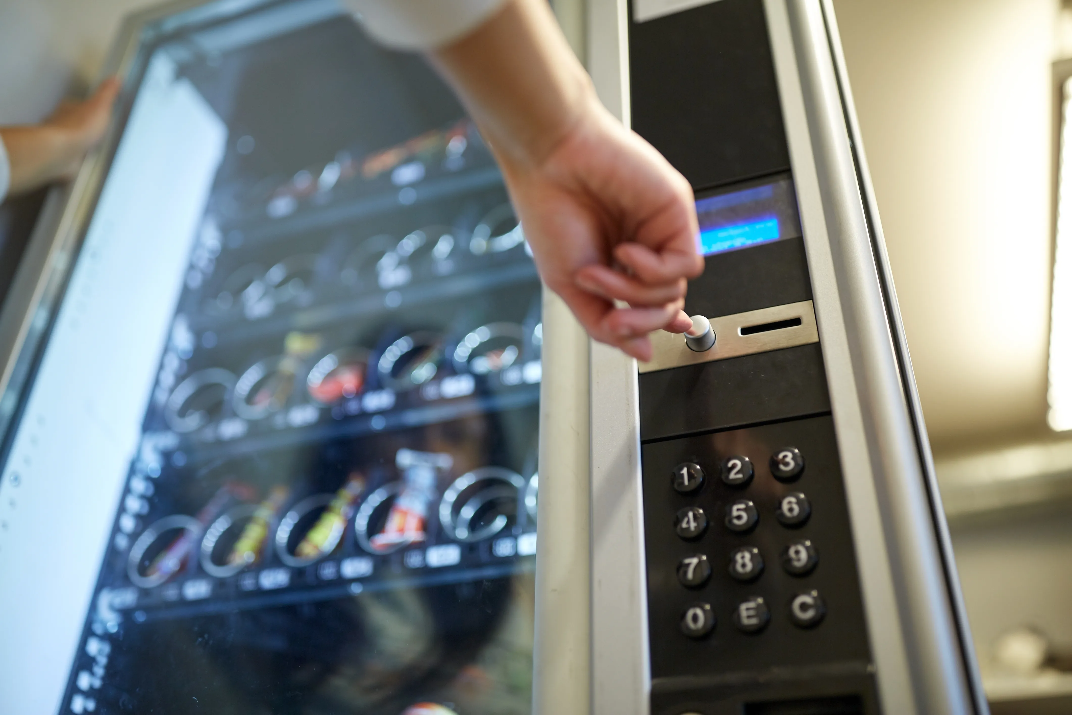 Main sélectionnant un produit sur le clavier d'un distributeur automatique de boissons et de snacks