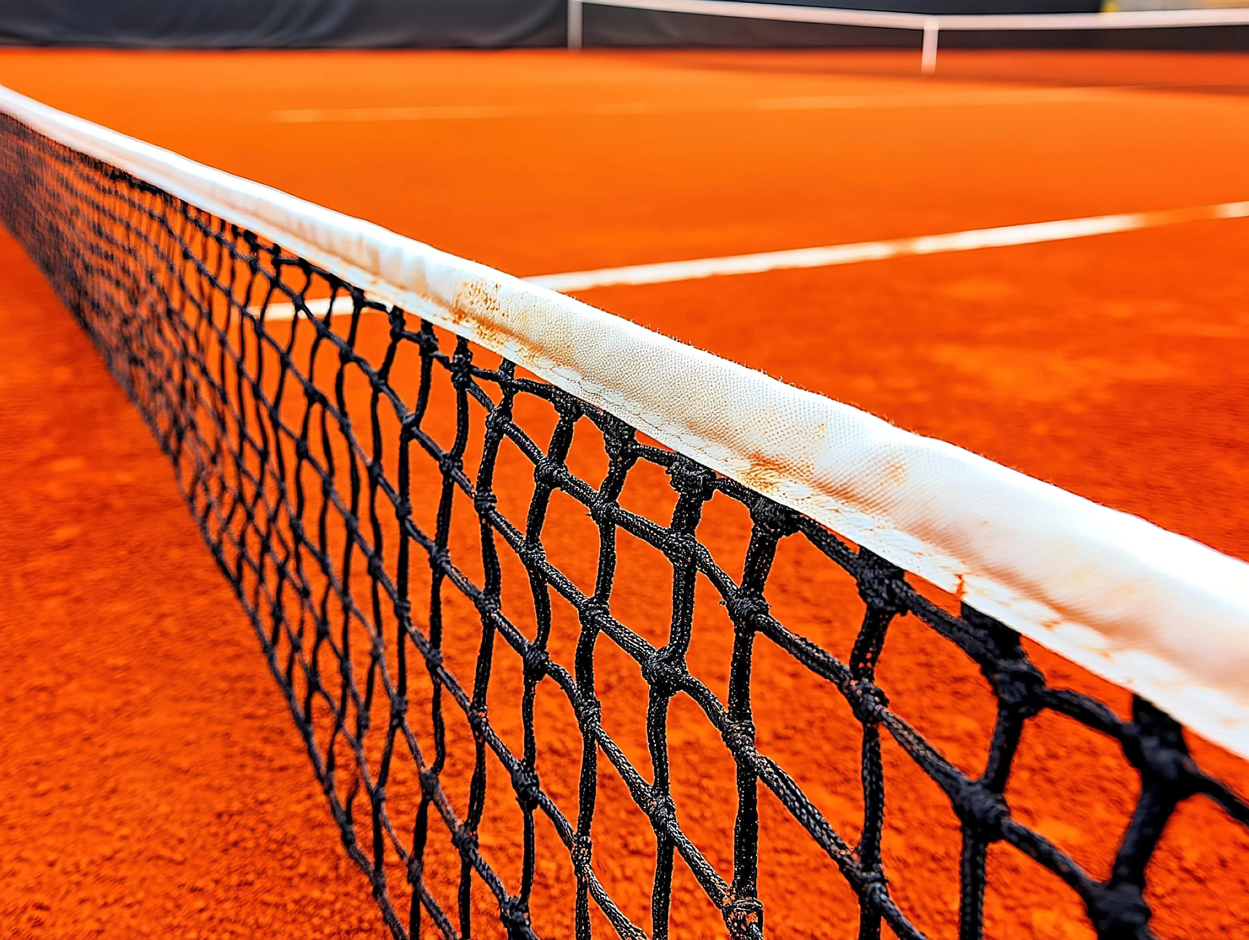 Gros plan sur le filet et les lignes blanches d'un terrain de padel à la surface orange